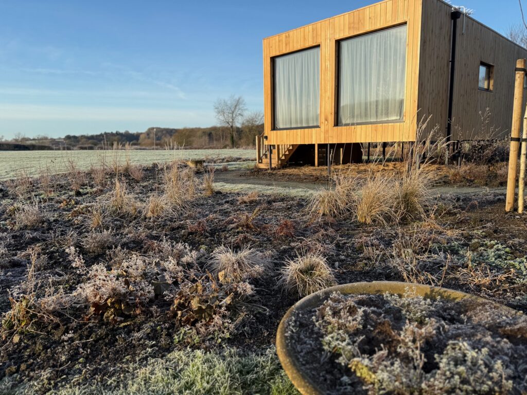 Exterior of a luxury self-catering lodge at Unbox Poplar Tree in Durham, featuring floor-to-ceiling glass windows and cedar cladding, overlooking open countryside.